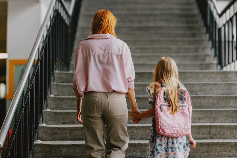 Mother guiding her young daughter to school up the stairs, symbolizing back to school season and family bonding.