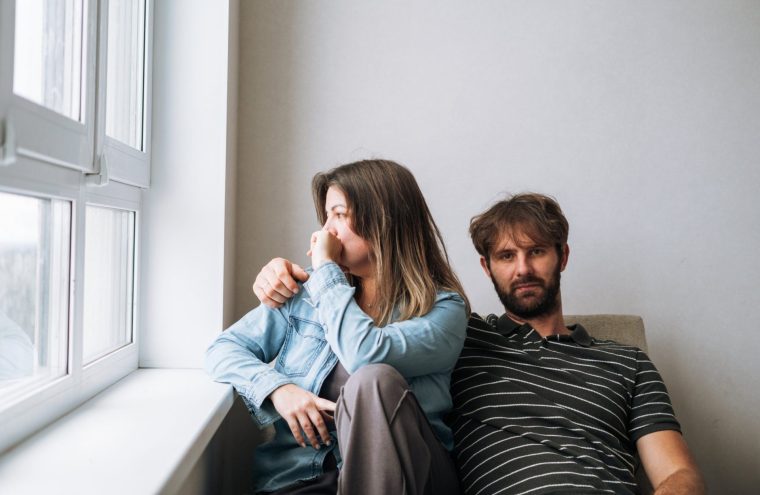 A married couple sitting in silence, looking in opposite directions. The image captures the concept of female loneliness within a marriage, emotional disconnection, and relationship problems. Symbolizes quiet desperation and isolation at home