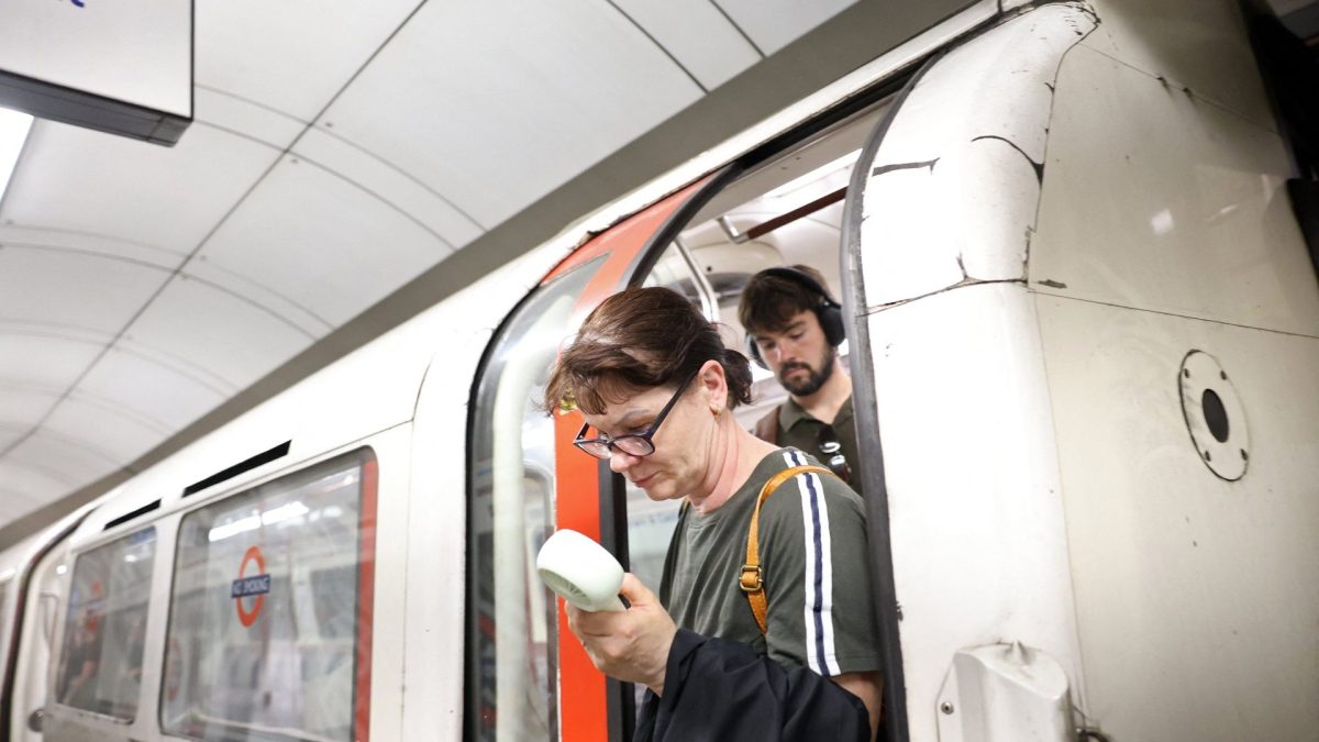 A commuter uses a fan in an attempt to cool down, as they exit a London Underground tube carriage, in London on June 23, 2026. Multiple schools in England shut early on June 23 and set to remain closed for two more days with a heatwave expected to set new records in the UK as it spreads across Europe. (Photo by Toby Shepheard / AFP via Getty Images)