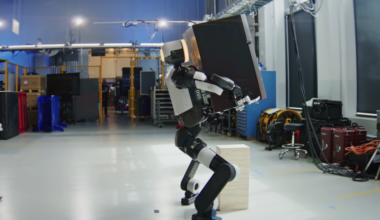 An Atlas humanoid robot developed by Boston Dynamics crouches as it lifts a mini fridge.