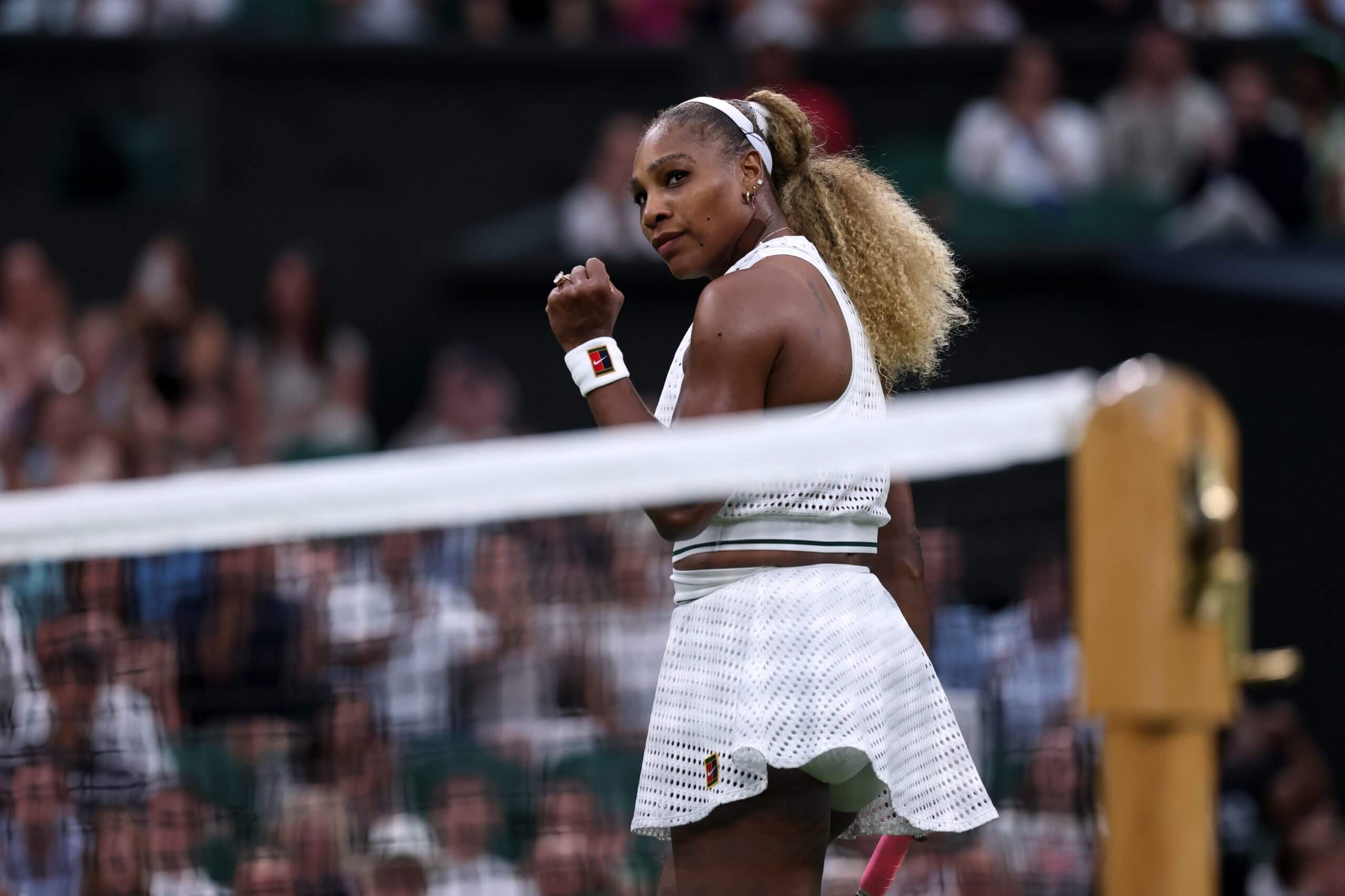Serena Williams pumps her fist next to a tennis net.