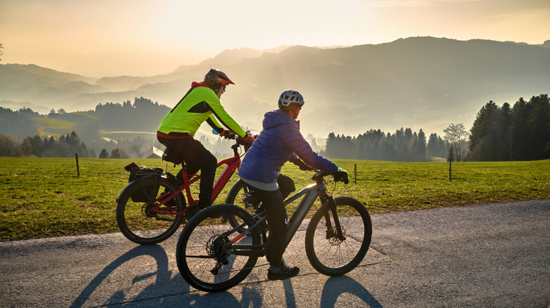 Two cyclists pedal past a mist-shrouded valley as the sun rises