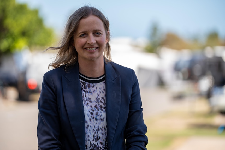 Emily Bourke smiles and stands in a car park with the wind in her hair and a smile on her face