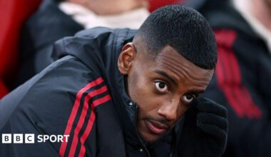Alexander Isak looks on from the bench in a zip-up dark jacket with red stripes before the Champions League game between Liverpool and PSV Eindhoven at Anfield on 26 November, 2025