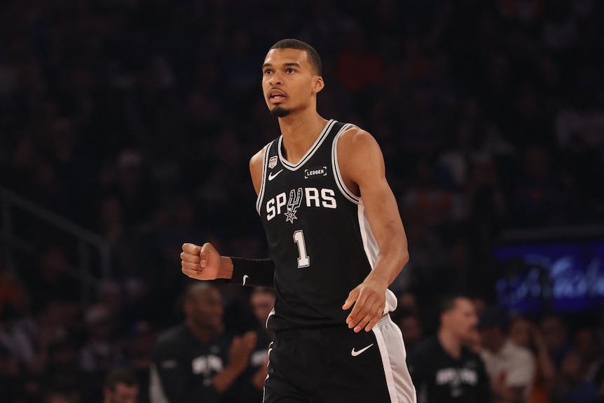 A basketballer walking backwards on the court, pumping his fist.