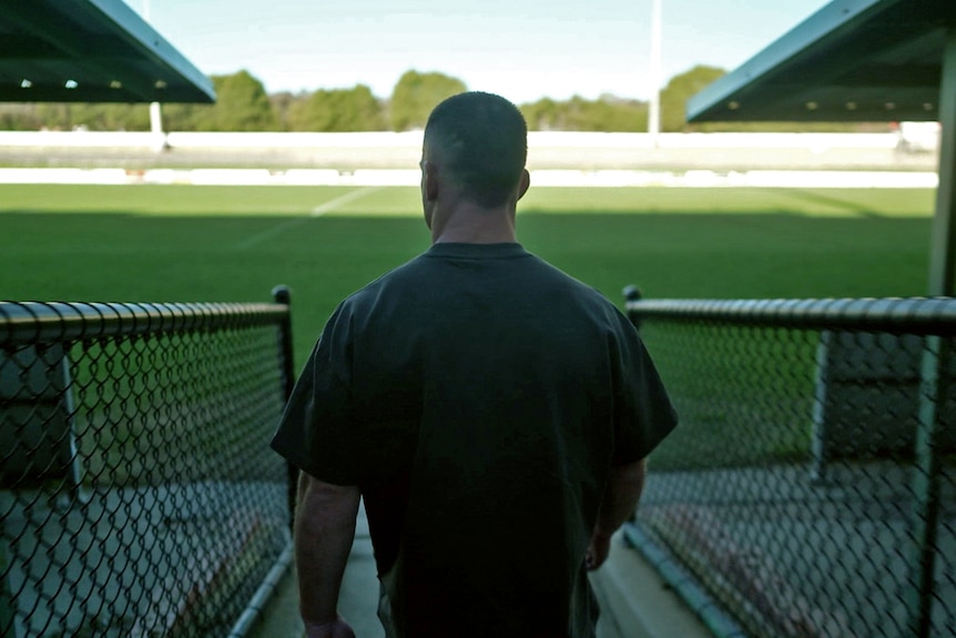A shot of the back of a man as he walks towards a large green football field.