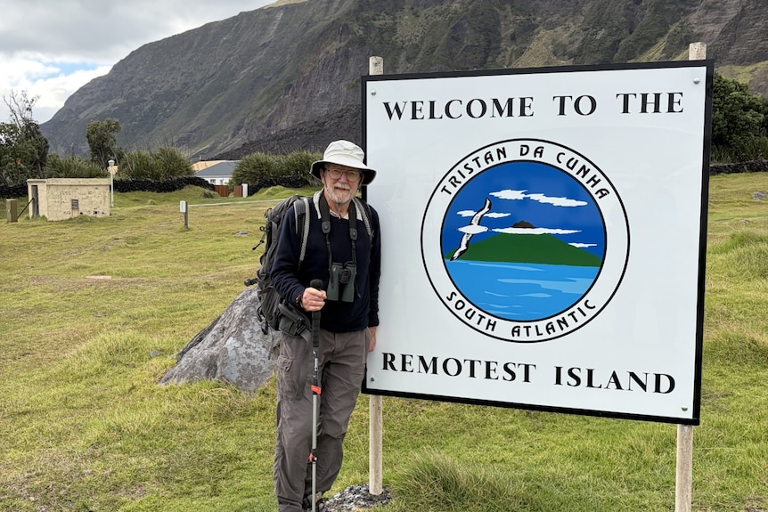 An elderly man stands in front of a tourist sign.