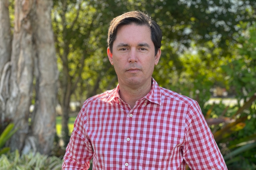 A man in a red and white shirt looks seriously towards camera