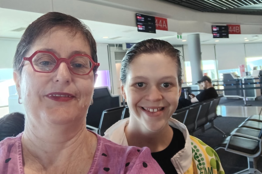 A woman and her teenage daughter talking a selfie at the airport.
