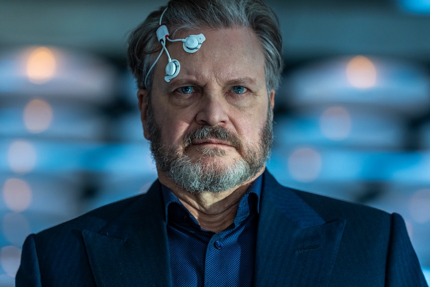 An older man with a device on his head looks at the camera