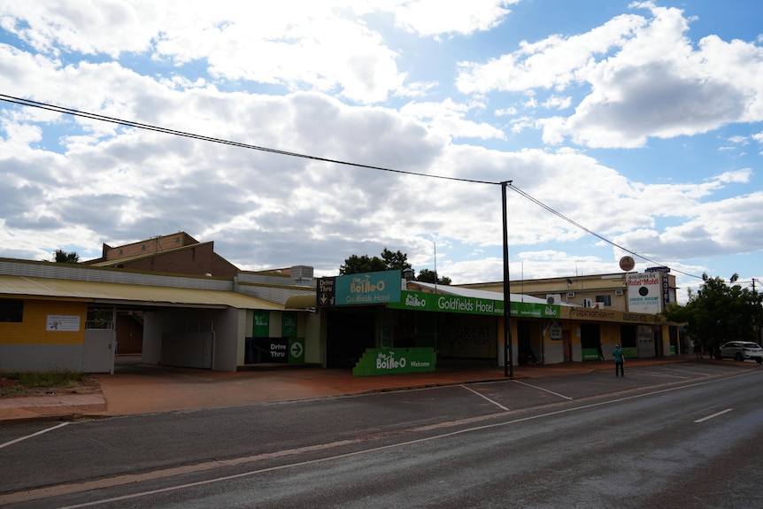 A wide shot of a street in a small town, with only a few cars seen edge of frame and one person walking.