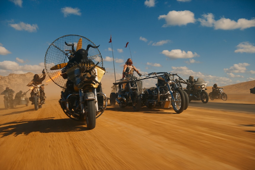 Film still of a bunch of modified motorbikes charging through the desert at speed.
