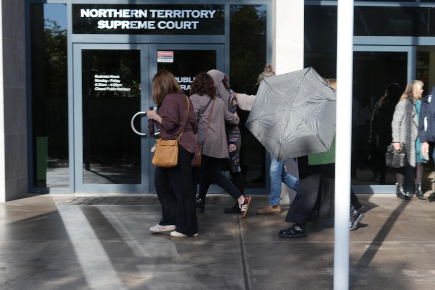 A group of people leaving the Northern Territory Supreme Court, they surround a woman in an attempt to hide her identity.