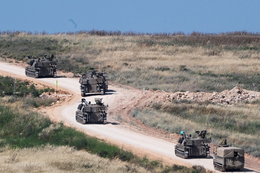 A convoy of military vehicles driving down a dirt road in a grassy plain.