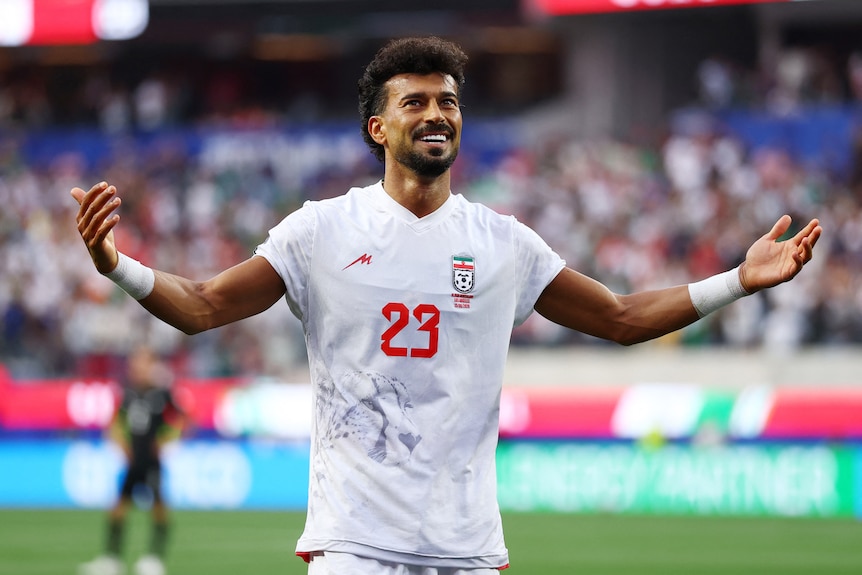 Iran player Ramin Rezaeian smiles and holds arms outstretched after scoring a goal