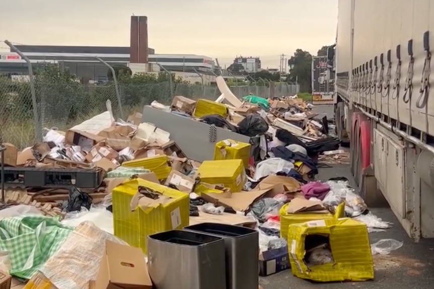 A truck in a parking bay, with massive amounts of household waste piled up along the fenceline.