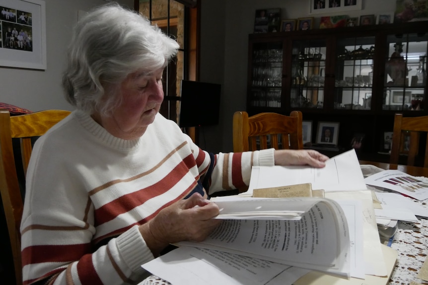 A woman in a white jumper with red and orange stripes looks through a book.