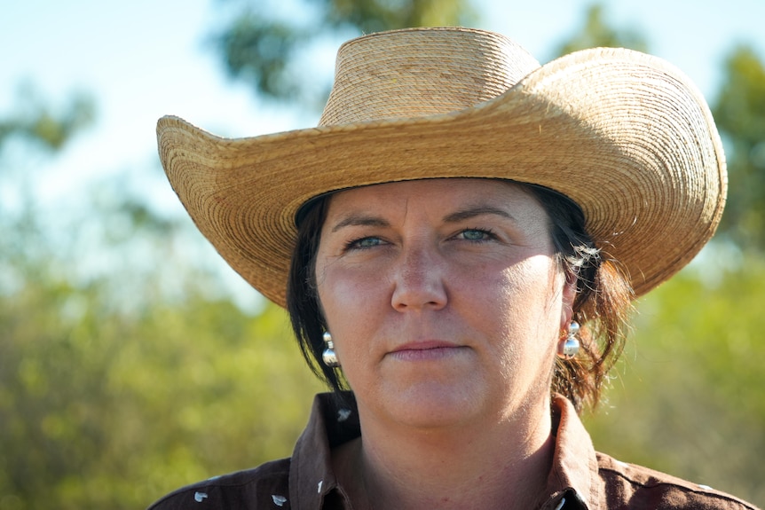 A woman with a large, cowboy style hat , with shrubs in background
