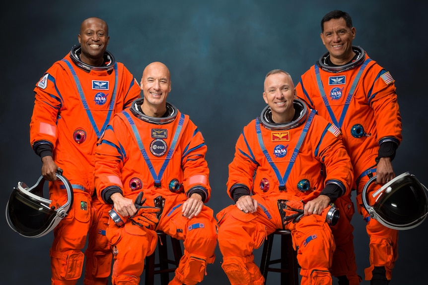 Four astronauts pose for phot in orange suits