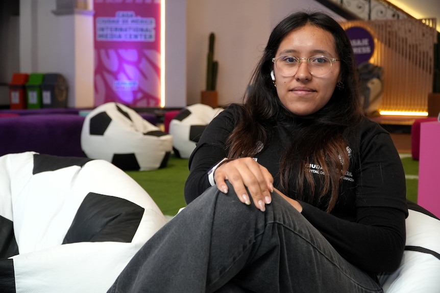A young woman with long brown hair and glasses sits on a soccer beanbag