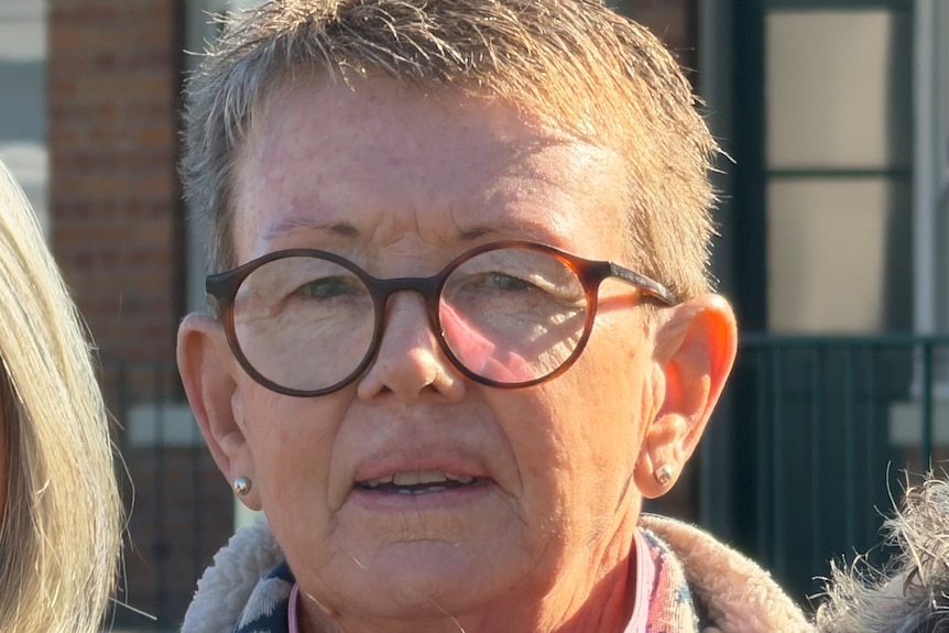 A woman with short hair into the camera while standing in a crowd.
