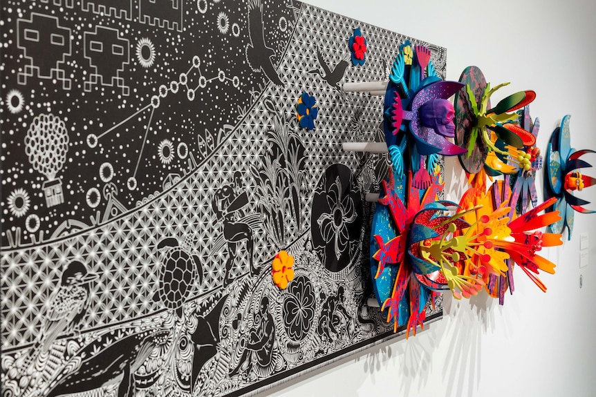 A black and white lino-cut adorned with colourful flower-like sculptural elements.
