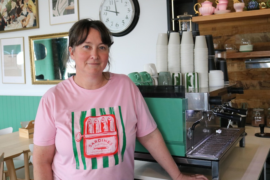 A woman standing next to a coffee machine in a cafe.