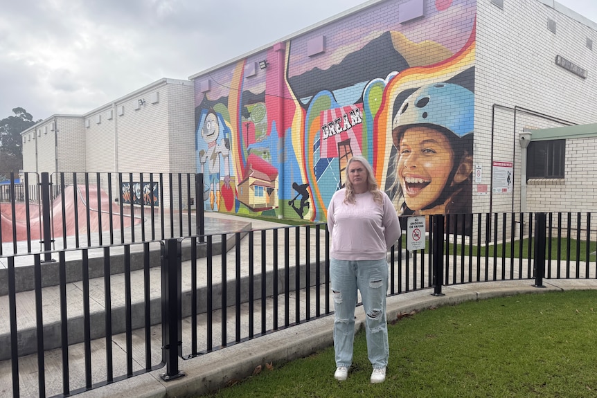 A woman standing next to a fence for a skate park.