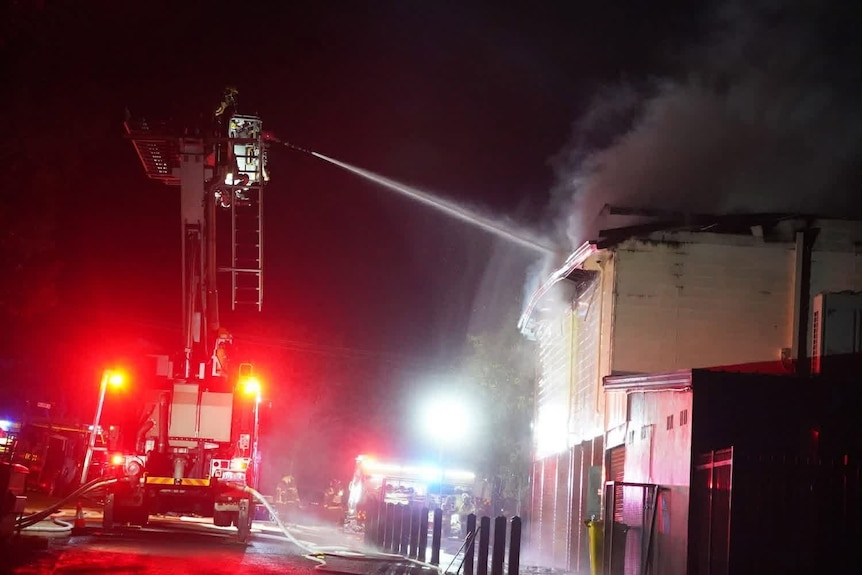 a burning two story building being hosed down by a firefighter in a cherrypicker