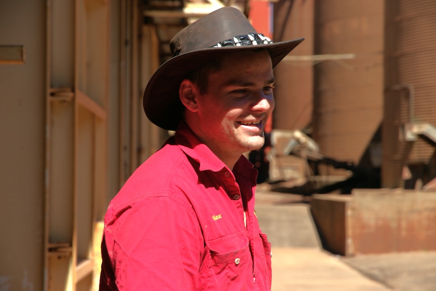 Man in red workshirt and wide brimmed hat smiling at peanut processing plant.