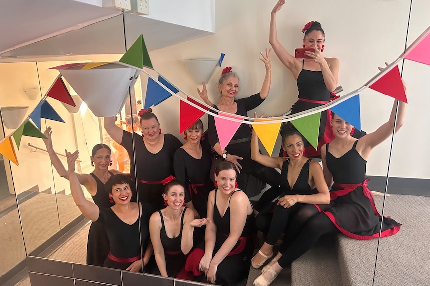 A group of female dancers dressed in black in a stairwell hung with colourful bunting.