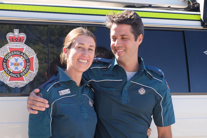 two paramedics smiling, man smiling at the woman in front of a ambulance car