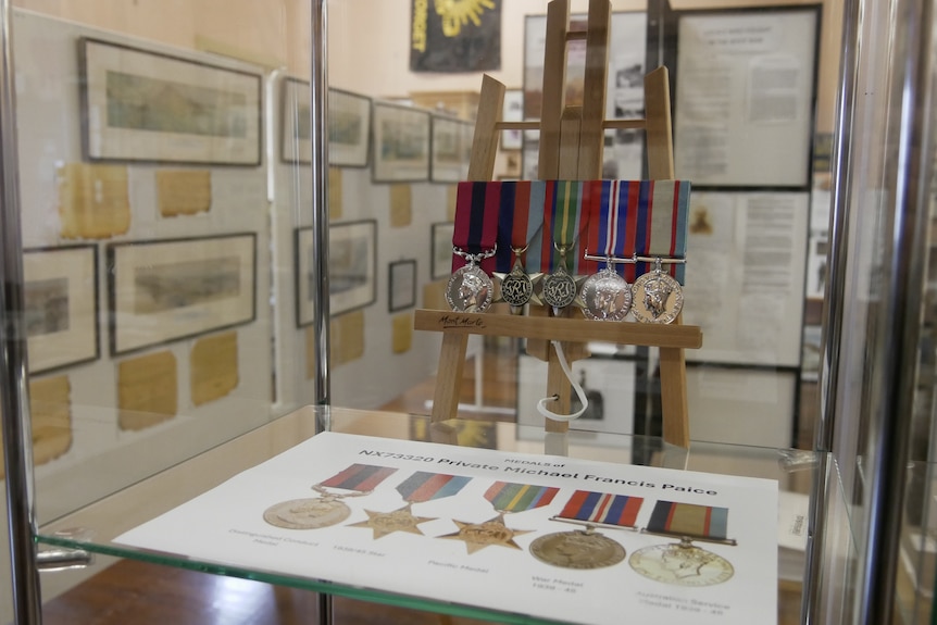 A glass case with a war medal pin with five medals inside of it.