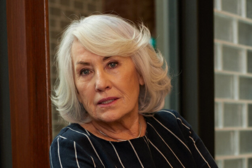 Ms Neilson with white hair cut in a bob looking at the camera with a neutral expression beside a window.