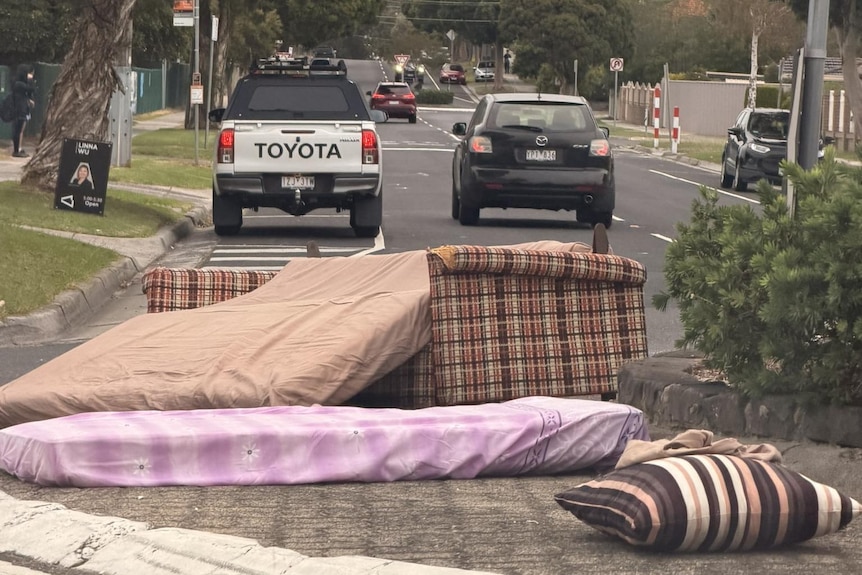 A couch and several mattresses and pillows, in the middle of a roundabout on a road.