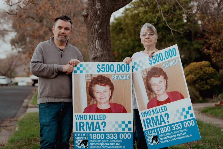 A man and a woman holding large signs advertising a $500,000 reward for a missing woman.