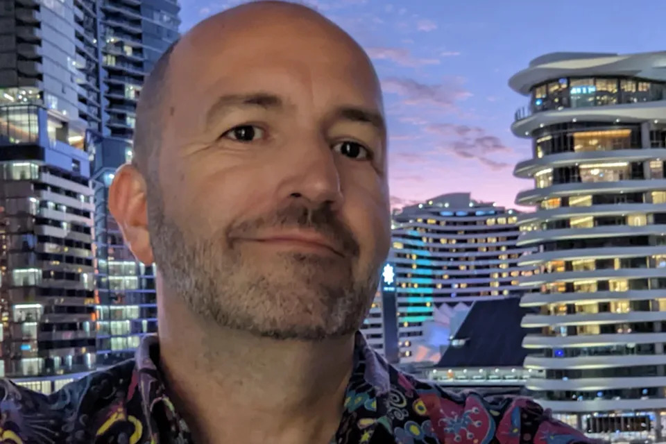Angus Kidman taking a selfie standing in front of buildings.