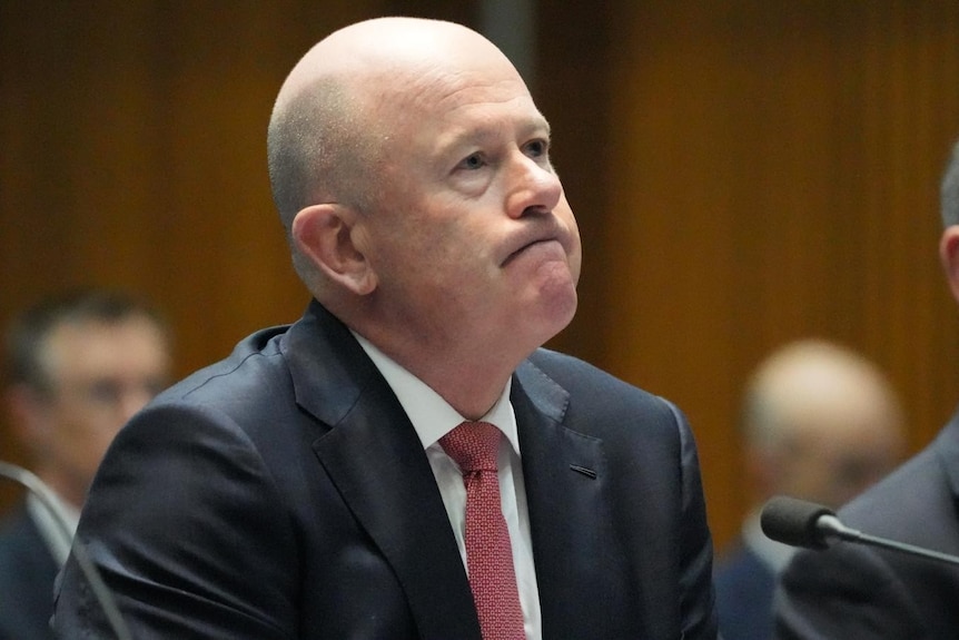 A bald man in a suit and tie purses his lips.