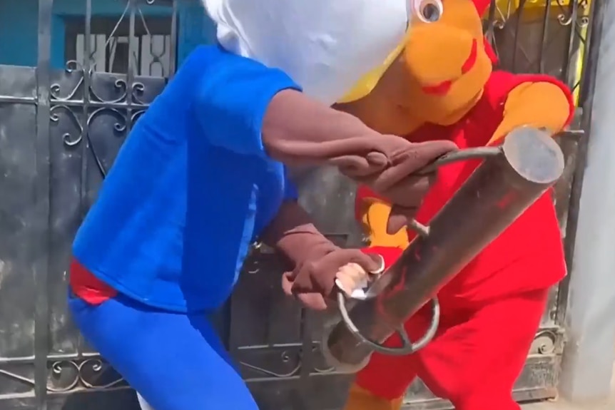 Two men in colourful costumes smash down a metal door.