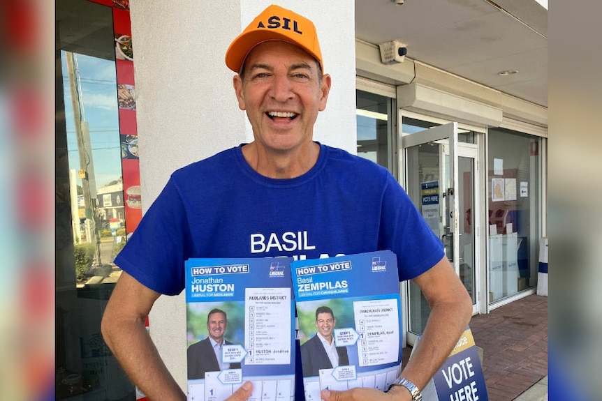 A man in a hat holding two political advertisments