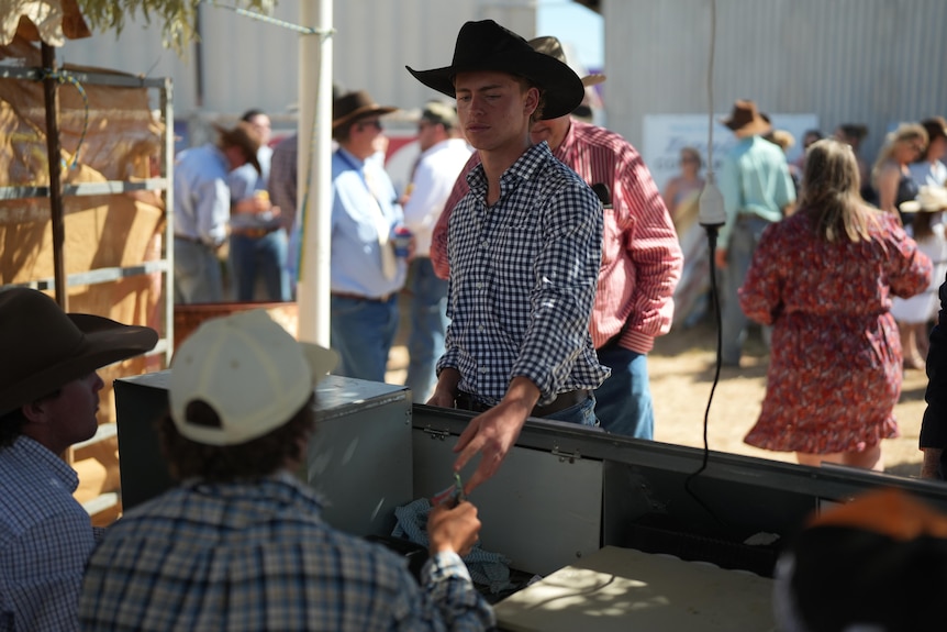 A man in a cowboy hat buys betting tickets at the outback races