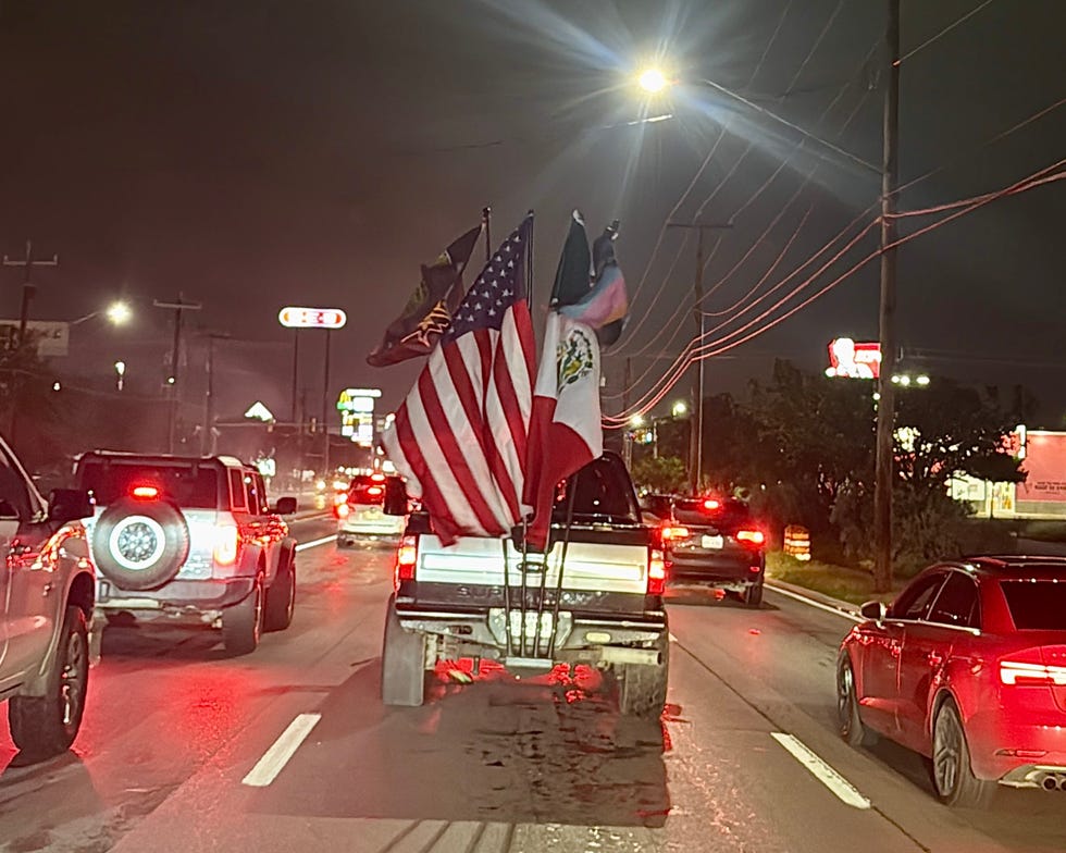 pickup truck displaying multiple flags driving on a road at night