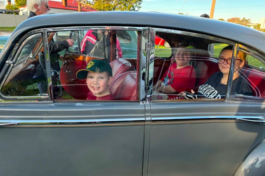 A smiling boy and two older firls sit in a vintage Volkswagen Beetle.