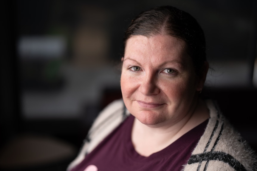 A woman wearing a maroon shirt and checked cardigan looks out.