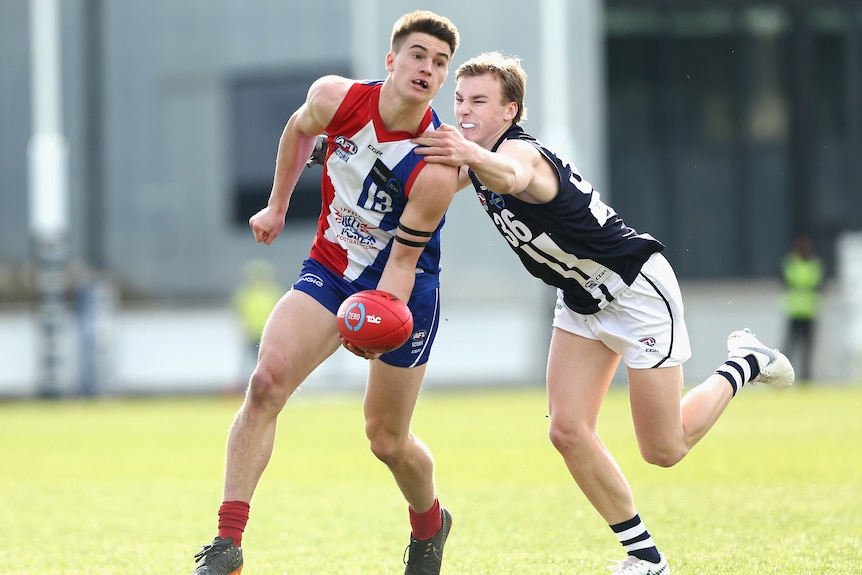 A photo of two AFL players mid-game. One is preparing to handball, the other is grabbing him.