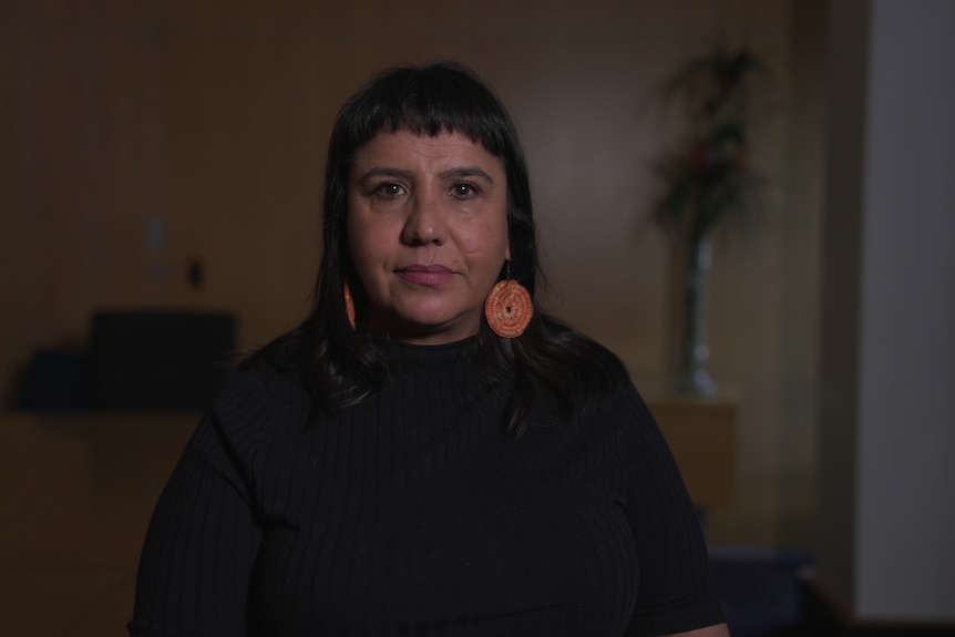 A woman wears dark clothing and large orange circle earrings as she looks forward.