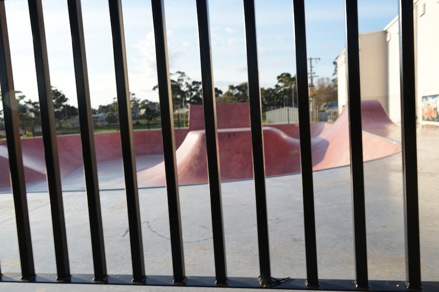 Pink skate park photographed through vertically barred black fence, like a jail cell.