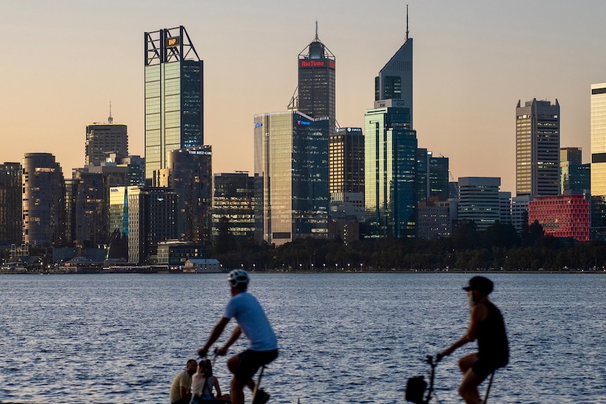 Skyscrapers in the background with the Swan River in the middle and two bicycle riders in the foreground.