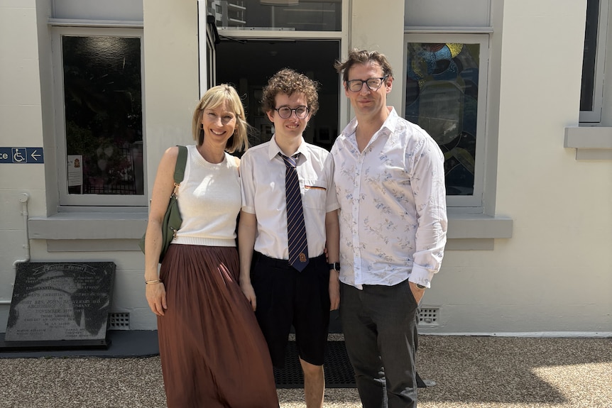 Three people, a woman and two men, standing next to each other and smiling.
