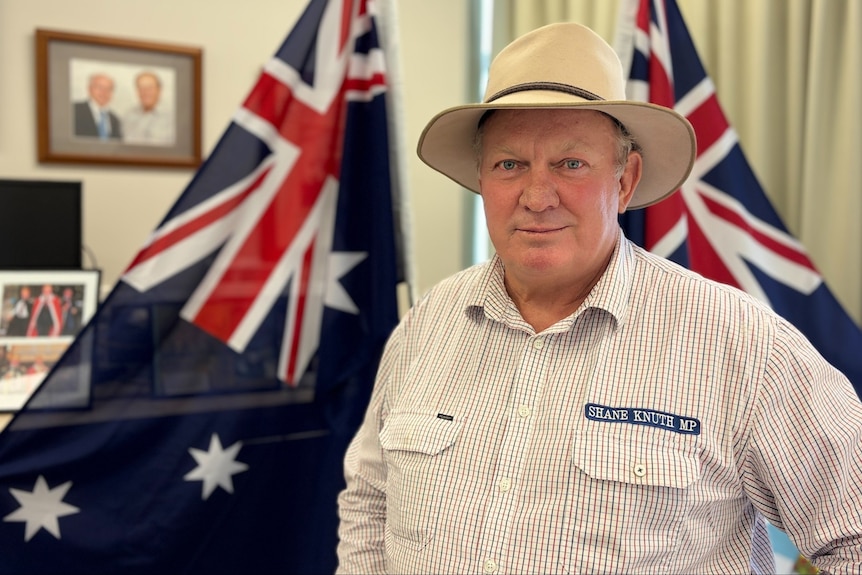 Man in wide-brimmed hat standing in front of Australian and Queensland flags